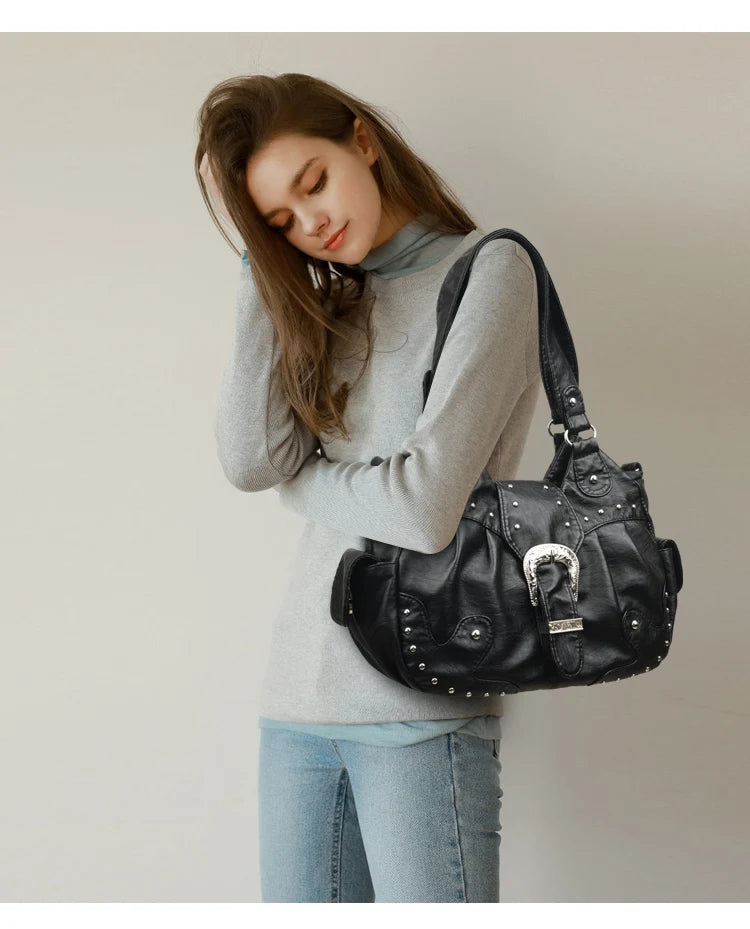 Eine Frau in grauem Rollkragenpullover und Jeans hält eine schwarze Vintage-Handtasche aus weichem Kunstleder.
