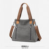 A gray canvas tote bag with brown leather straps and hardware shown in a side view.