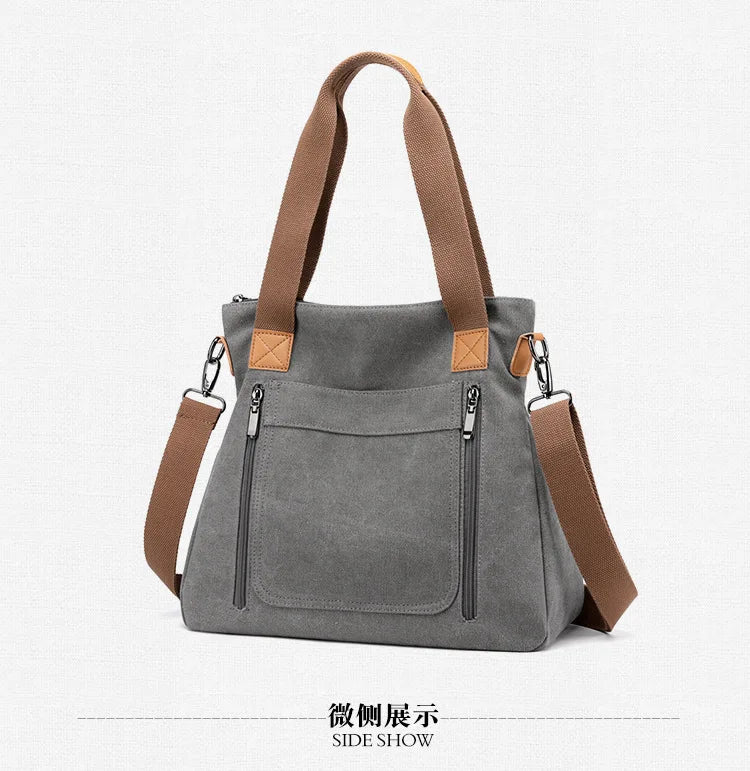 A gray canvas tote bag with brown leather straps and hardware shown in a side view.