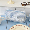 A striped blue and white cosmetic storage pouch with a white ribbon and lace trim resting on a light blue table.