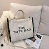 A white canvas tote bag with black trim is displayed against a soft, light background.