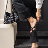 A person wearing dark pants is holding a black studded shoulder bag while standing on steps.