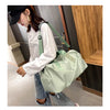 A woman is holding a light green nylon duffel bag with a black strap in an indoor setting.