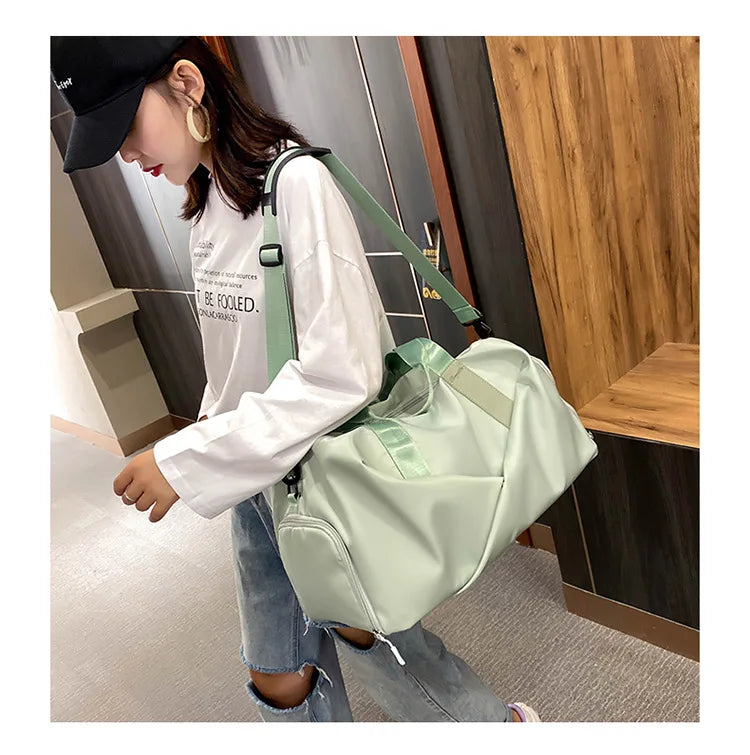 A woman is holding a light green nylon duffel bag with a black strap in an indoor setting.
