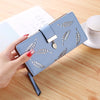 Cartera clutch de cuero PU azul claro con estampado de hojas grabadas, mostrada sobre una superficie de madera.