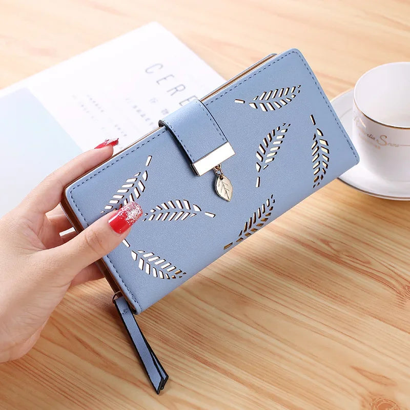 Cartera clutch de cuero PU azul claro con estampado de hojas grabadas, mostrada sobre una superficie de madera.