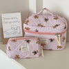 A pink and white striped bear cosmetic makeup bag resting on a light surface next to a sign.