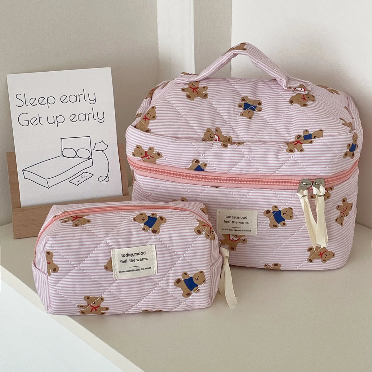 A pink and white striped bear cosmetic makeup bag resting on a light surface next to a sign.