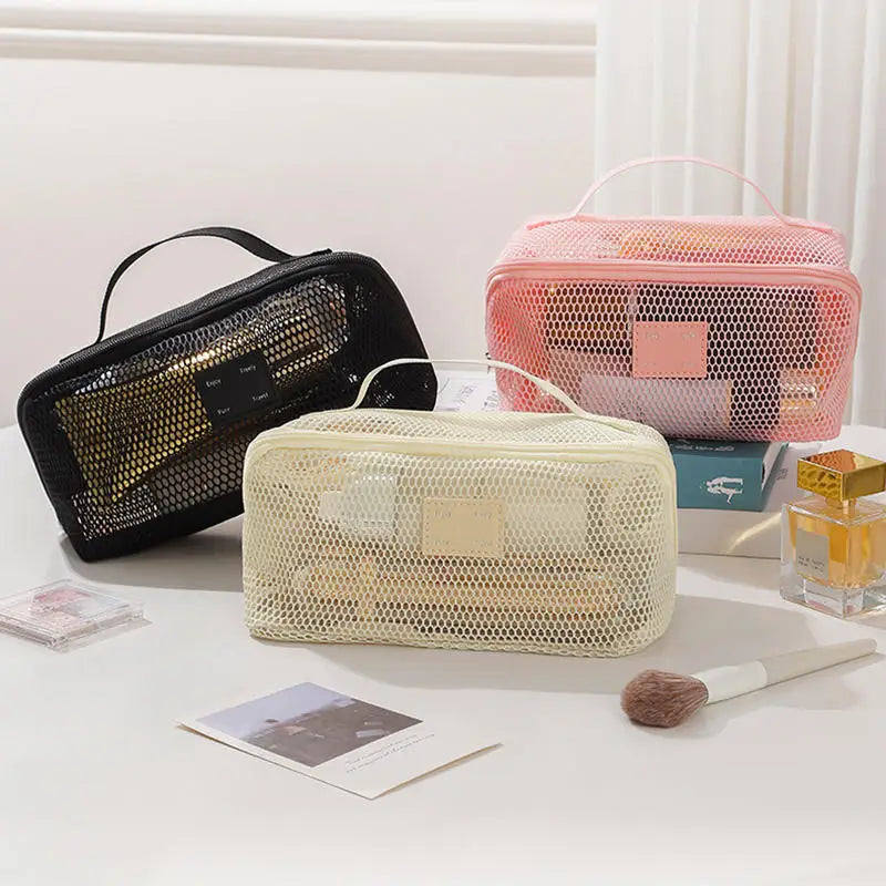 A collection of clear mesh cosmetic organizer pouches in pink and beige tones are displayed on a white surface.