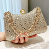 A hand holds a sparkling gold and diamond-inlay evening clutch bag with a pearl closure.
