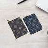 A dark gray zippered card holder wallet with a repeating geometric pattern is placed on a light wooden surface next to a whit