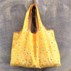 A bright yellow foldable reusable shopping bag hanging against a gray concrete wall.