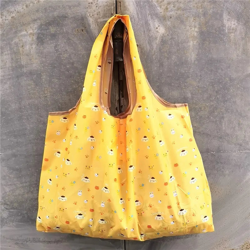 A bright yellow foldable reusable shopping bag hanging against a gray concrete wall.