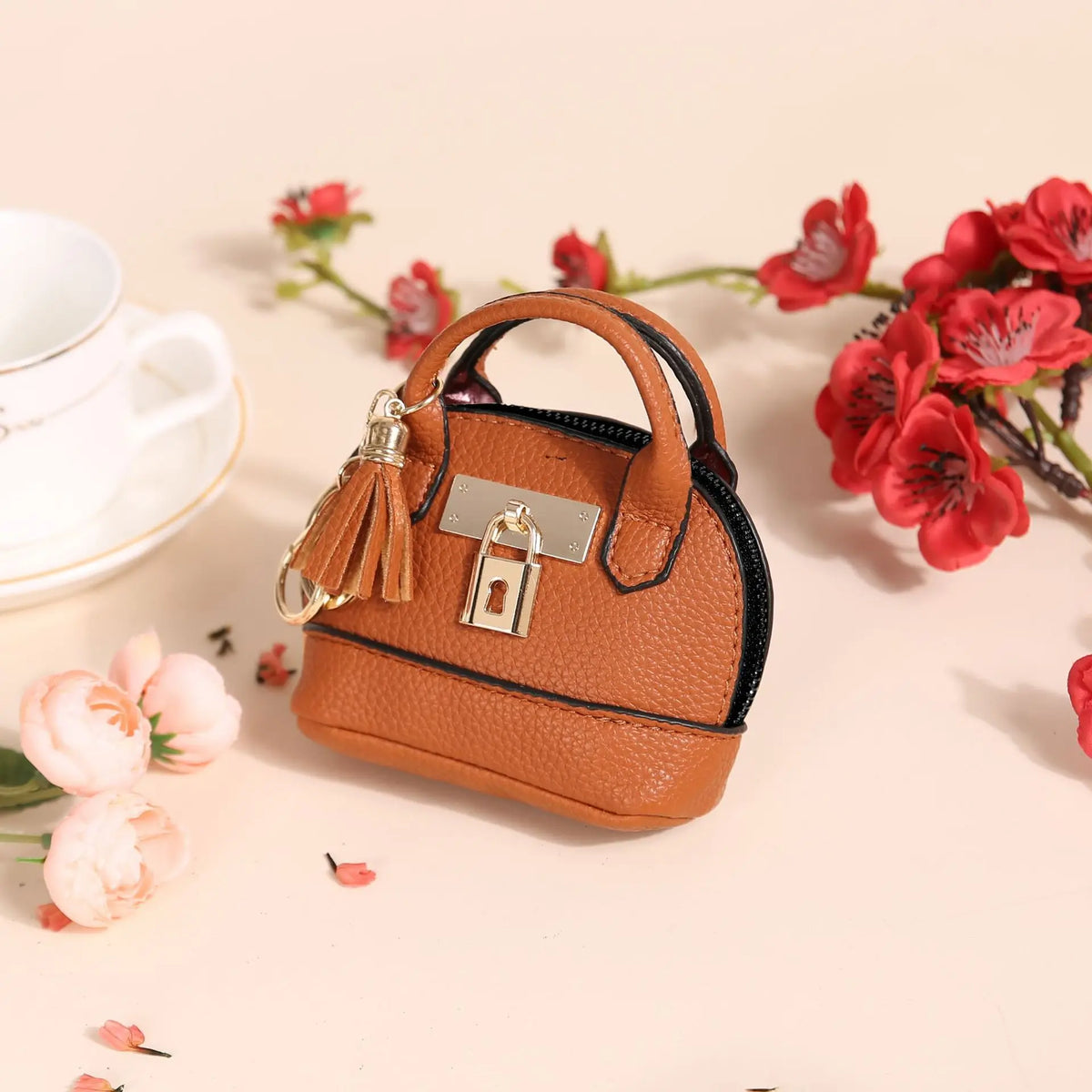 Petit porte-monnaie en cuir marron avec chaîne et cadenas, posé sur un fond clair avec des fleurs rouges.