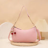 A pink leather shoulder bag with a gold chain and cherry pendant resting on a woven mat.