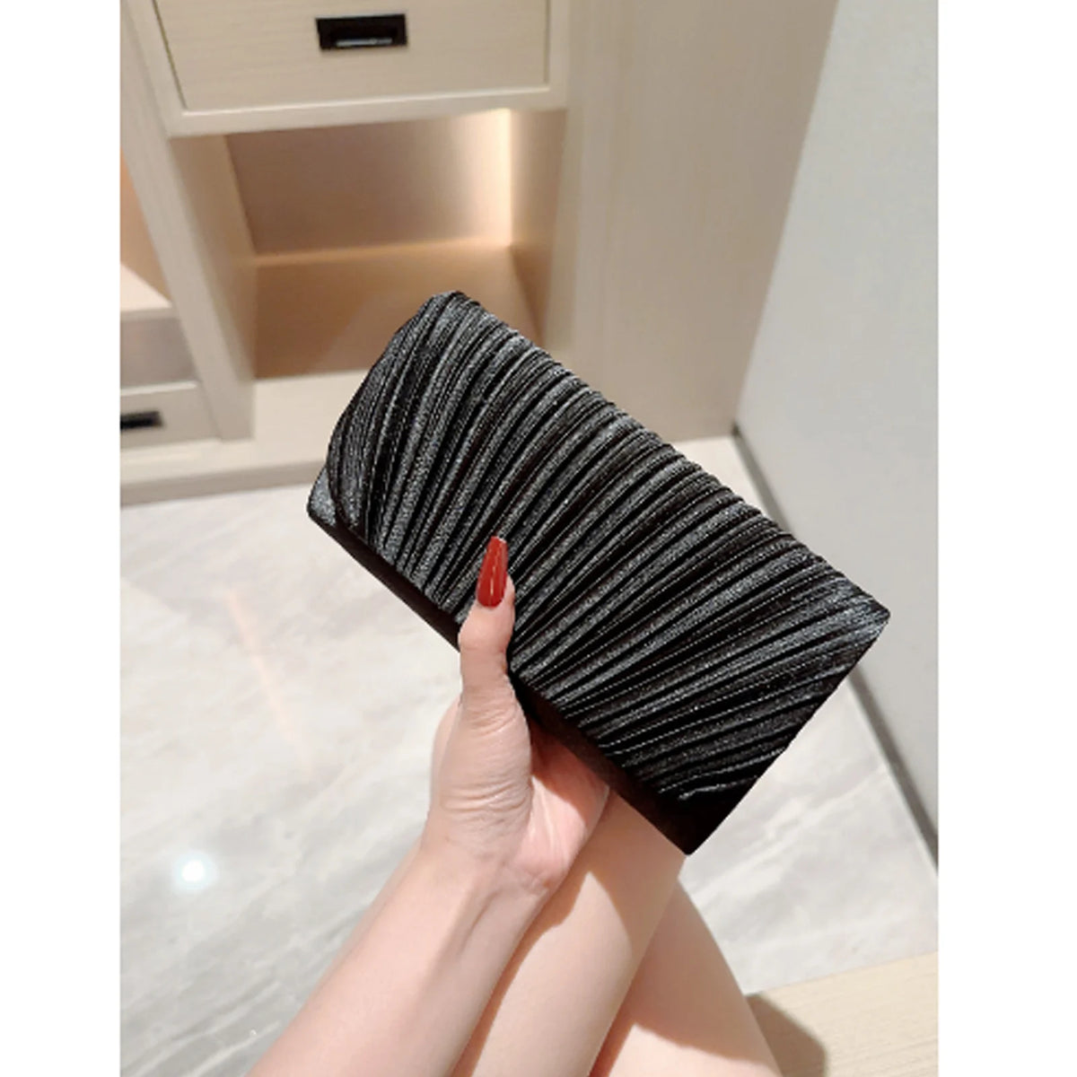 A close-up of a black textured chain shoulder clutch bag held by a hand.