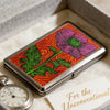 Art Deco metal card case with a floral design featuring pink and green flowers on a red background