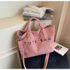 Un sac en toile côtelée rose avec une poignée est exposé sur une étagère à côté d'une pile de livres.