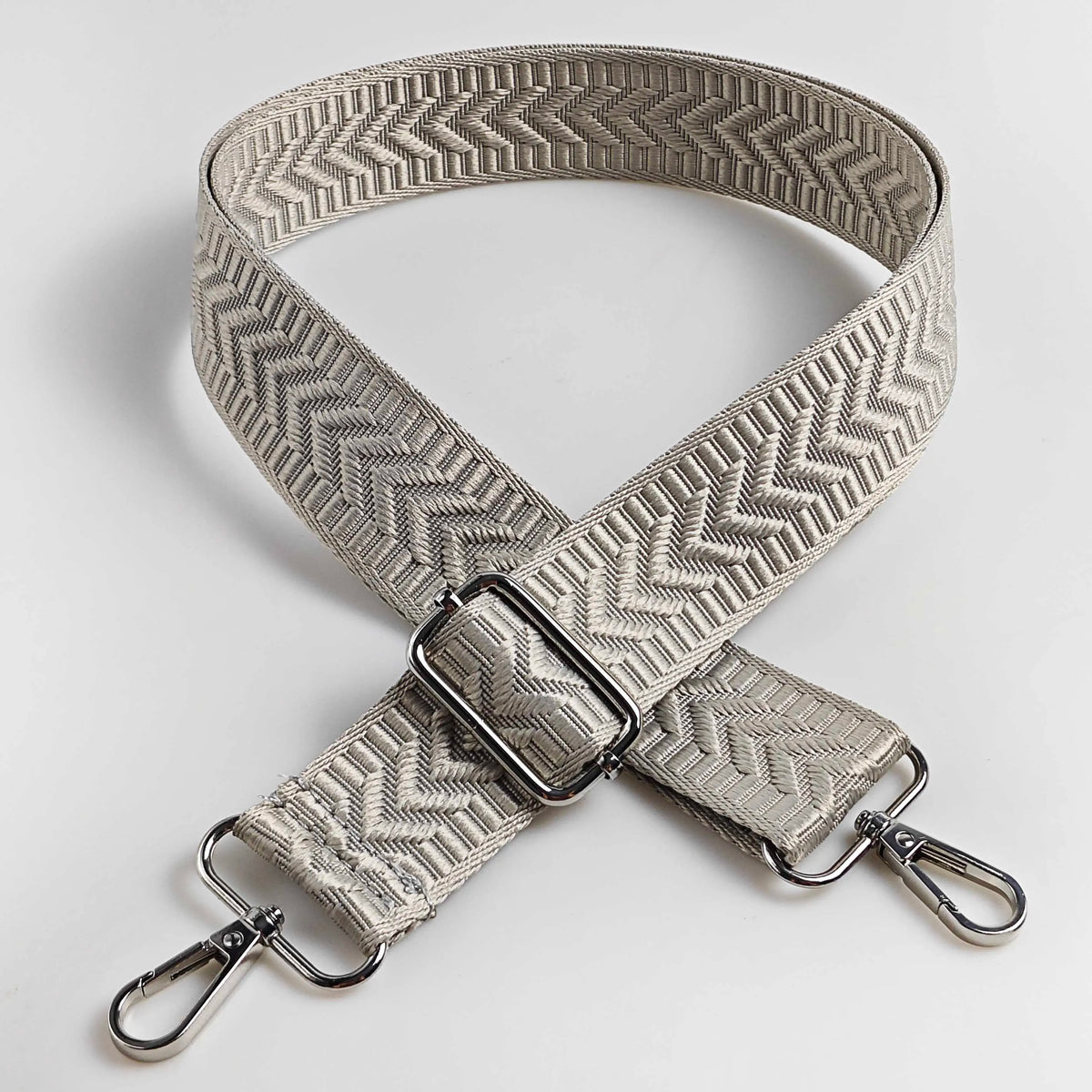 A beige woven leather handbag strap featuring an arrow jacquard pattern, shown in an X-shape.