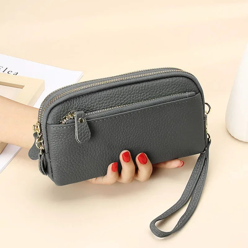 A dark gray genuine cowhide leather double-zip wristlet wallet is held in a hand on a light background.