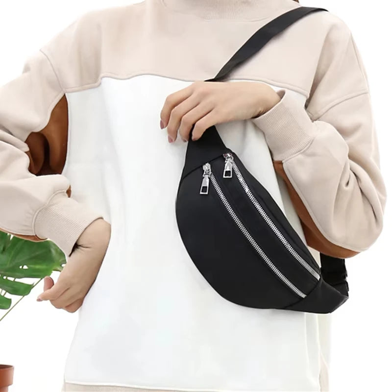 A beige sweater sleeve holds a black nylon crossbody sling bag with a silver zipper detail.