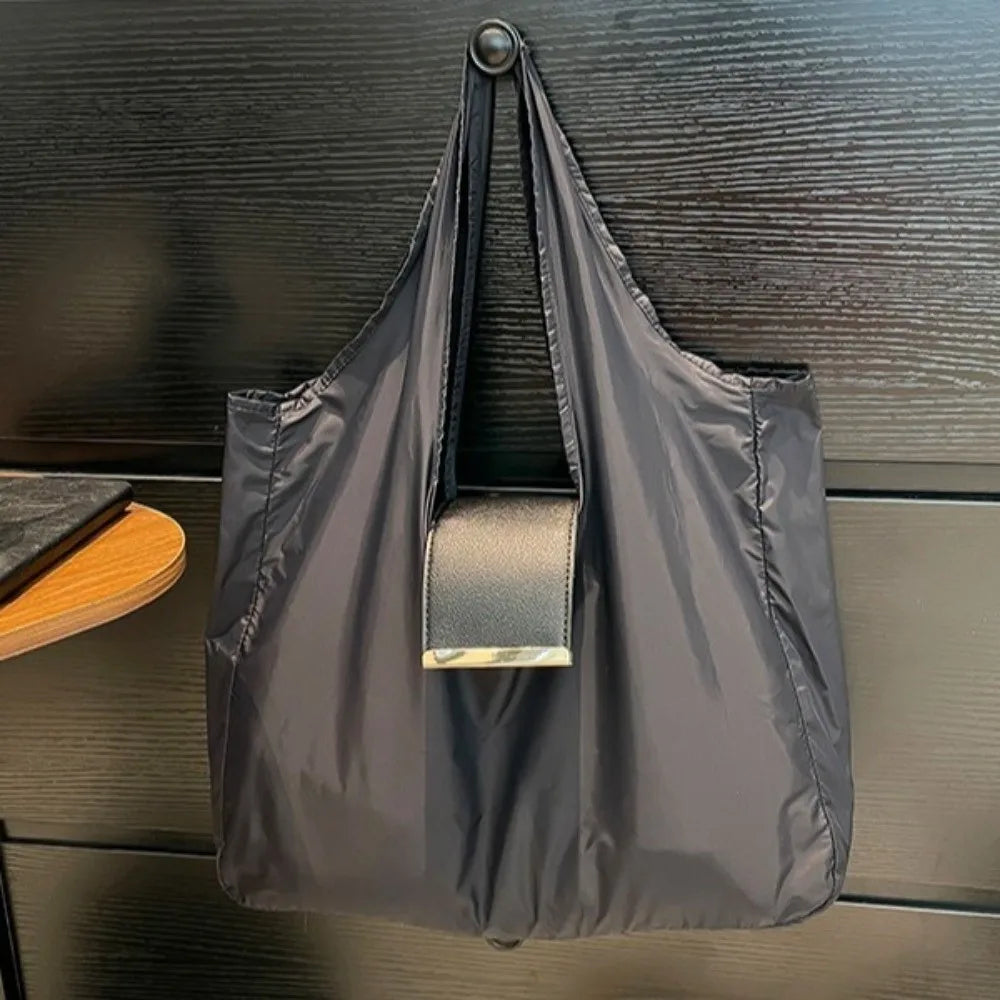 A dark gray reusable nylon mini keychain tote bag hanging on a wooden surface.