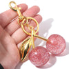Gold-toned keychain featuring a leaf charm and two round, glittery pink crystal fruit beads.