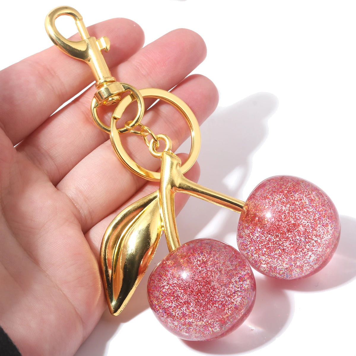 Gold-toned keychain featuring a leaf charm and two round, glittery pink crystal fruit beads.