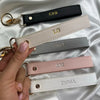 A hand holds several personalized leather wristlet keychains with gold hardware and various names engraved on them.