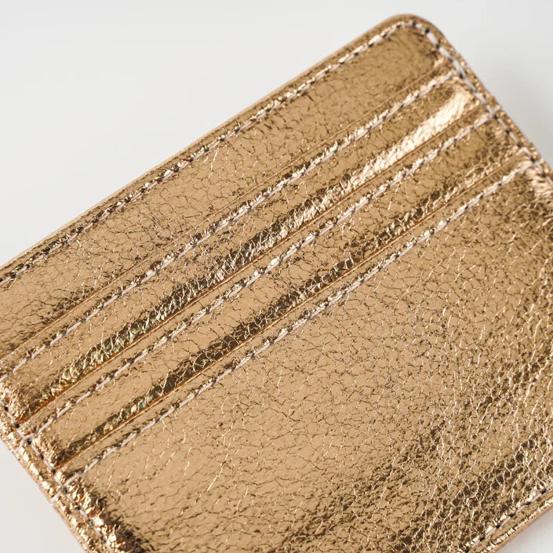 A close-up of a gold metallic leather mini wallet card holder with ribbed texture.