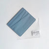 Porte-cartes en cuir véritable bleu clair avec un design plié, montré dans une pochette en plastique transparent.