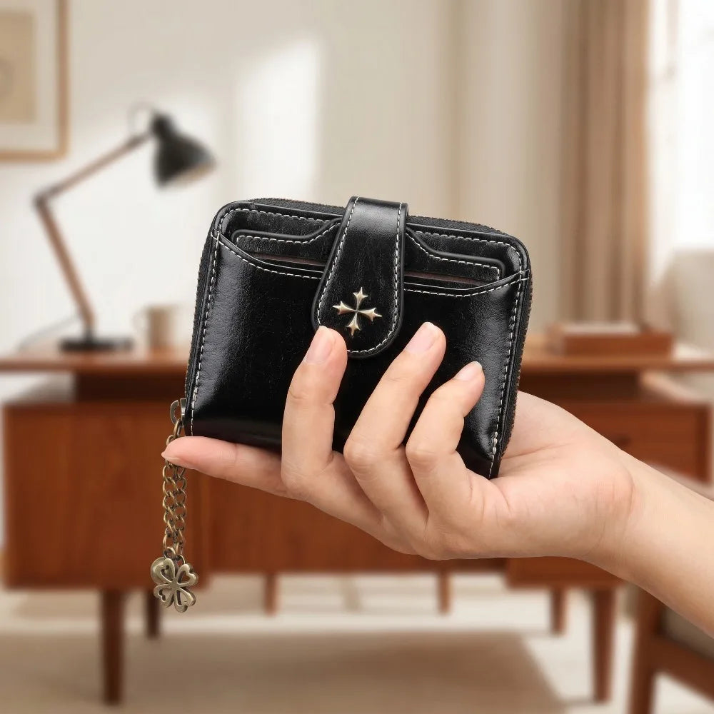 A hand holds a black leather mini wallet with a silver charm against a blurred indoor background.