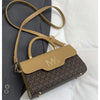 A tan Michael Kors letter square crossbody bag with a brown monogram pattern resting on a gray blazer.