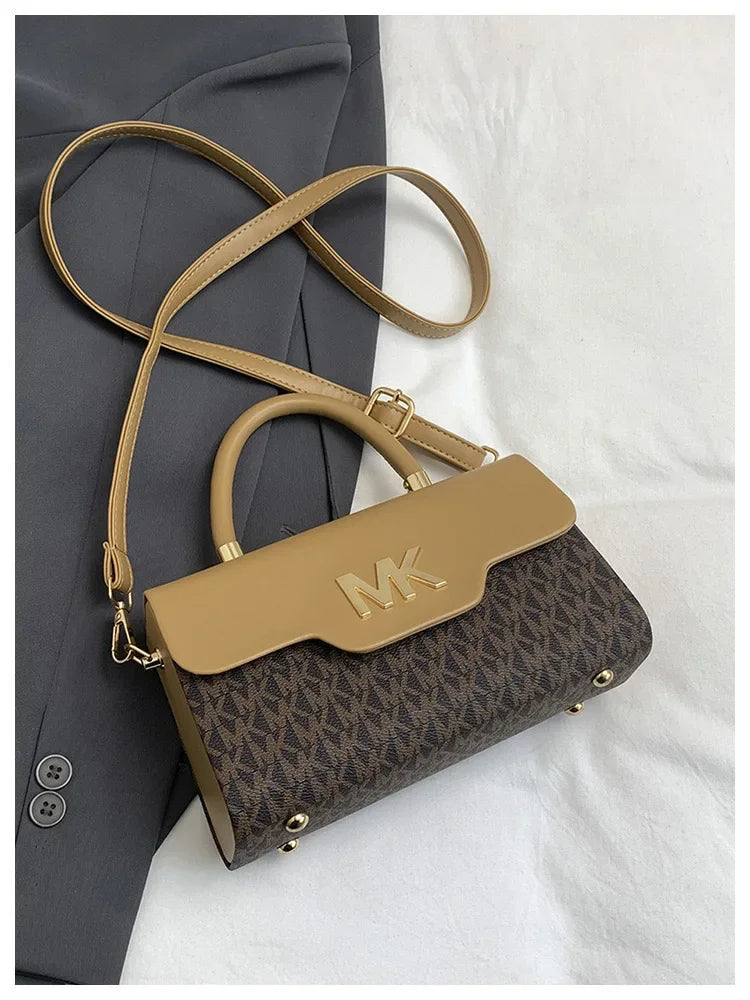 A tan Michael Kors letter square crossbody bag with a brown monogram pattern resting on a gray blazer.