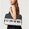 A black tote bag with white polka dots and piano lace trim is held by a woman.
