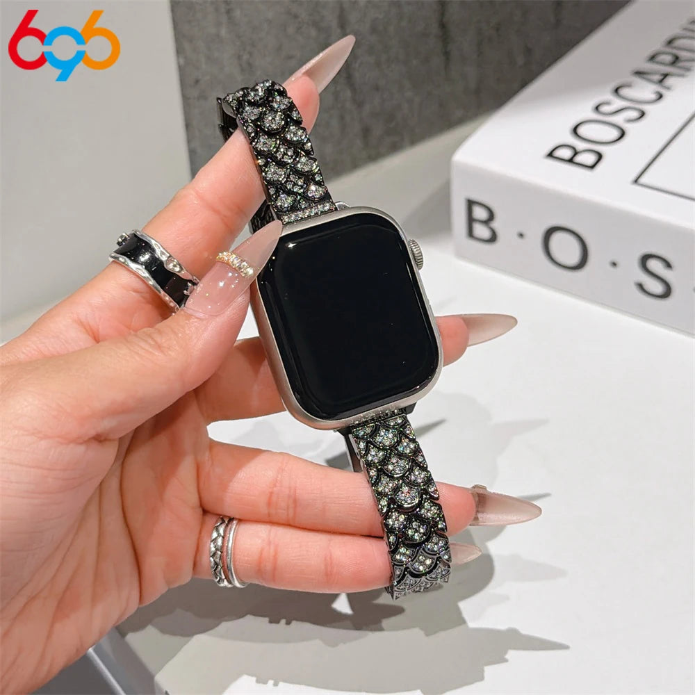 A hand is holding a black Apple Watch with a sparkling metal strap featuring crystal fishscales.