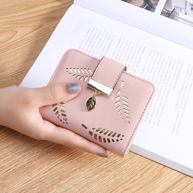 Una mano sostiene un bolso clutch de cuero PU rosa con detalles dorados sobre una superficie de madera.