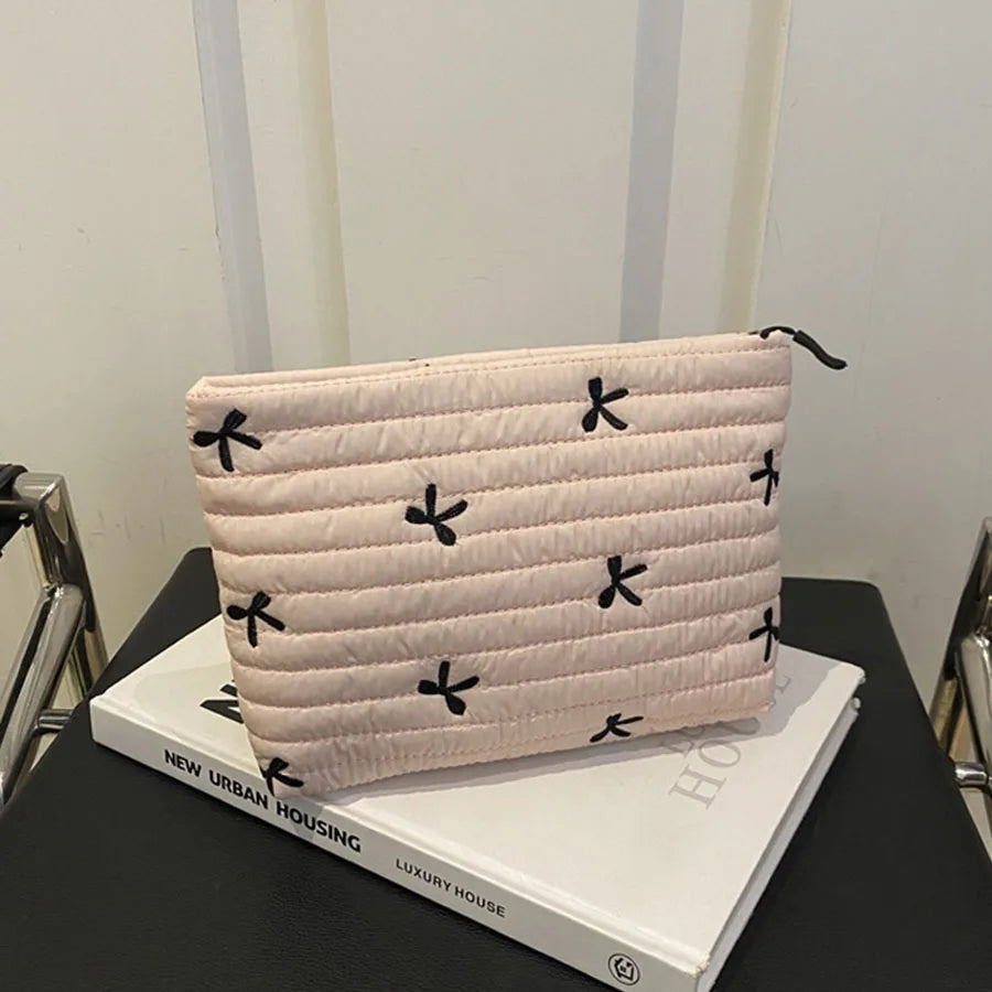 A light pink quilted makeup pouch with black embroidered motifs resting on a white book.