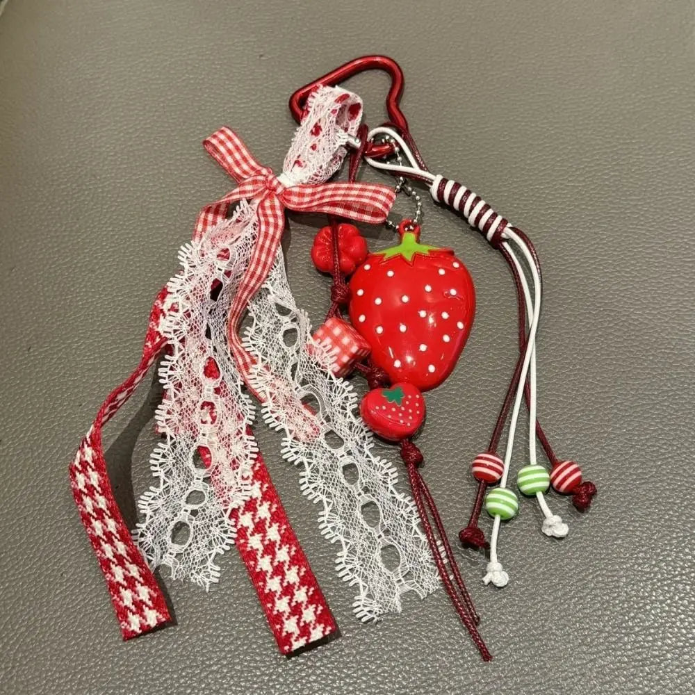 A red strawberry bag charm keychain featuring a fabric bow and white lace details.