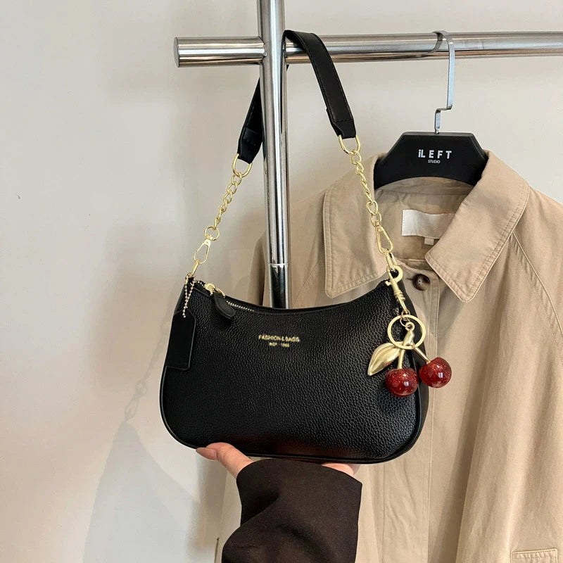 Black leather shoulder bag with gold chain and cherry pendant hanging on a hanger.