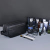 A black premium PU leather toiletry bag is shown with various grooming products and tools on a gray surface.
