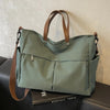 A light sage green nylon tote bag with brown straps and multiple internal pockets resting on a dark surface.