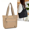 A beige canvas tote bag with black straps and zippered pockets shown next to a person.
