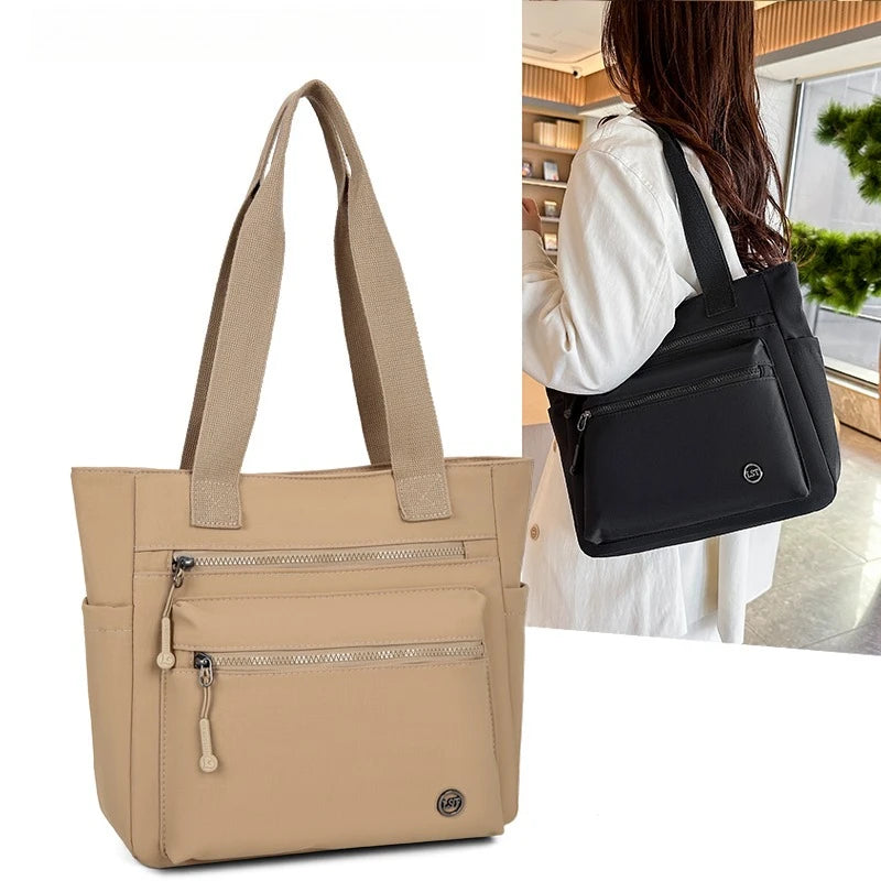 A beige canvas tote bag with black straps and zippered pockets shown next to a person.