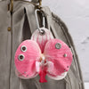 A pink and white orchid flower keychain attached to a gray fabric bag.