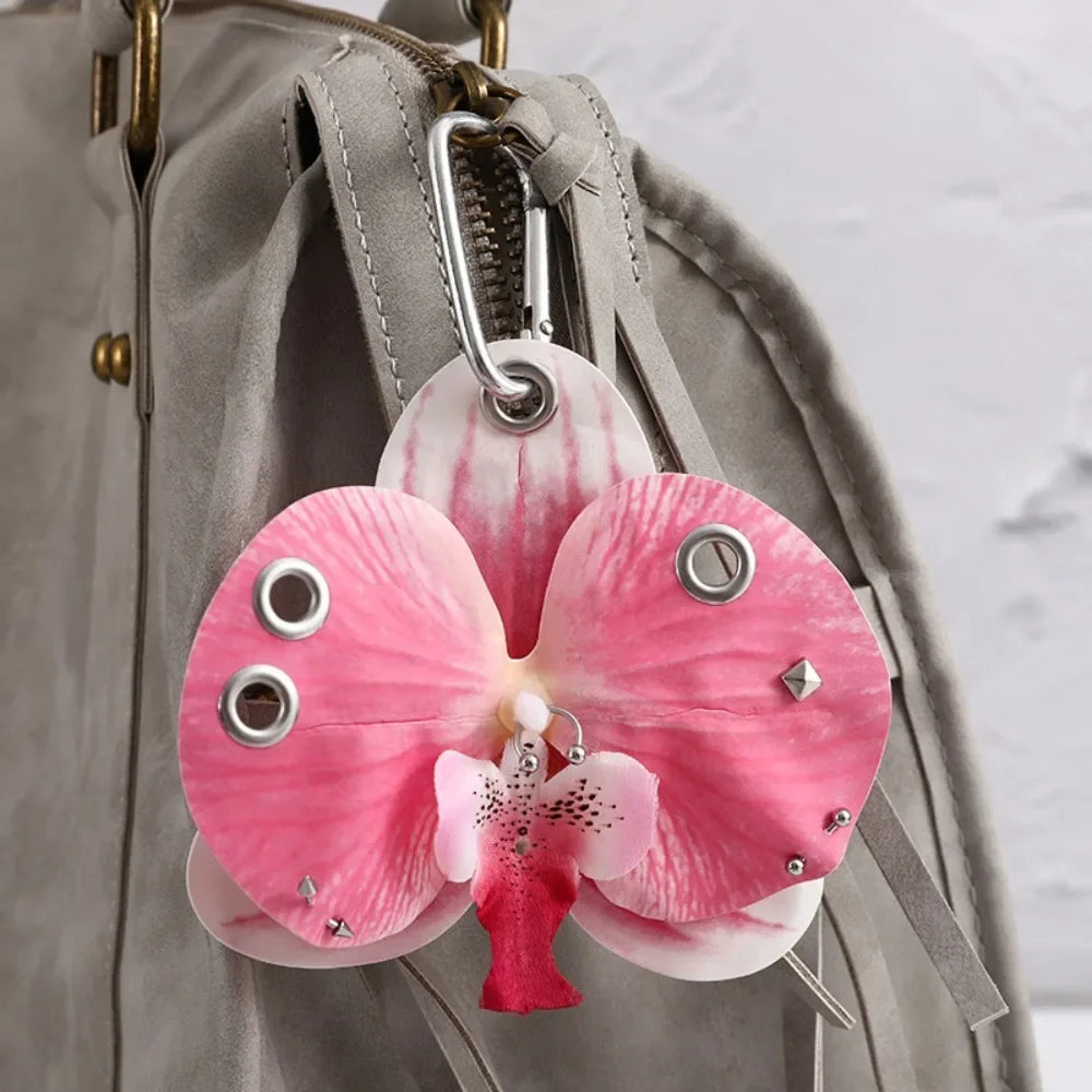 A pink and white orchid flower keychain attached to a gray fabric bag.
