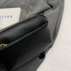 A close-up of a black vegan PU crossbody bag with a gold zipper on a gray fabric background.