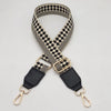 A close-up of an adjustable braided nylon bag strap featuring a black and beige checkered pattern and gold-toned metal hooks.