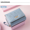 A light blue compact PU leather women's wallet with floral embroidery shown on a pink background.