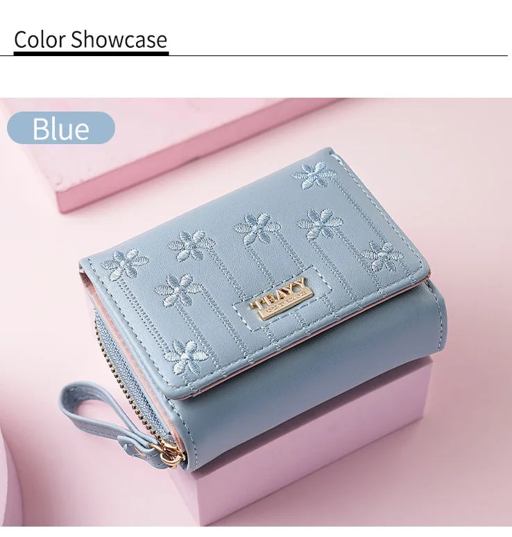 A light blue compact PU leather women's wallet with floral embroidery shown on a pink background.